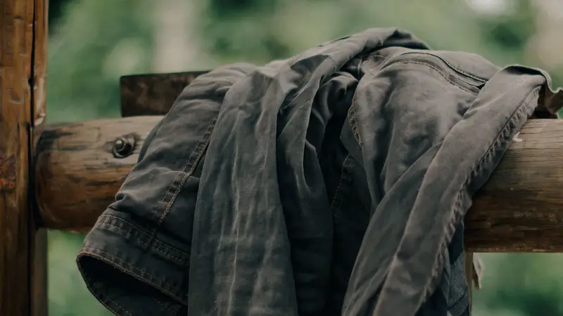 Worn, faded jacket hanging over a wooden fence rail in the woods